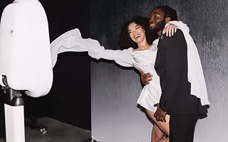 Couples posing in front of a heart-themed Valentine’s Day photo booth with romantic props and a red-and-pink floral backdrop, smiling as their photos print instantly.