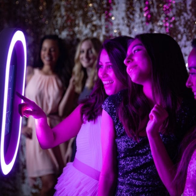 Elegant open air photo booth setup at an evening wedding with guests taking portraits.