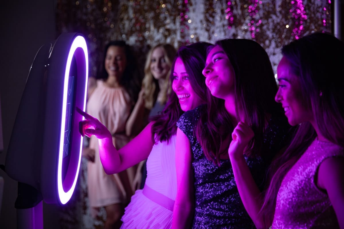 Elegant open air photo booth setup at an evening wedding with guests taking portraits.