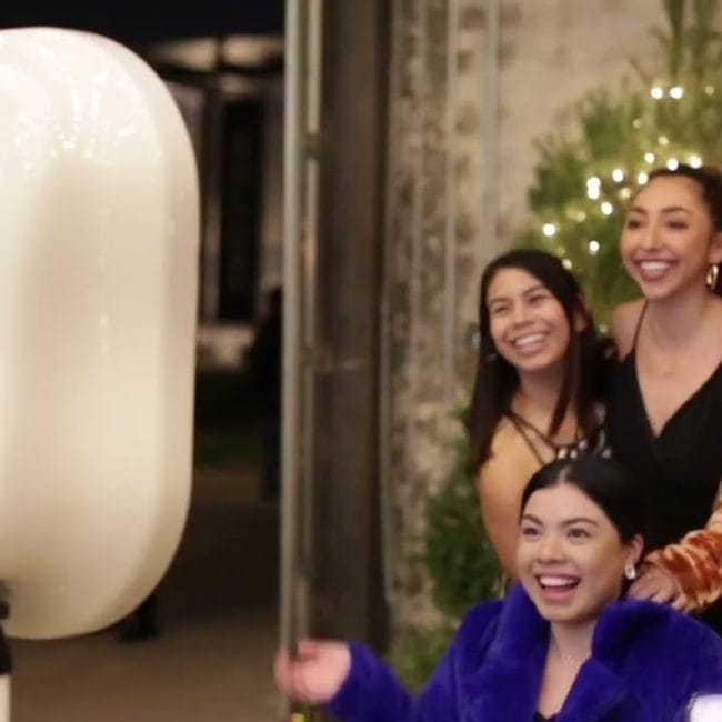 Guests laughing and posing in front of a winter-themed photo booth at a corporate holiday party in Metro Detroit, with twinkling lights and festive props.