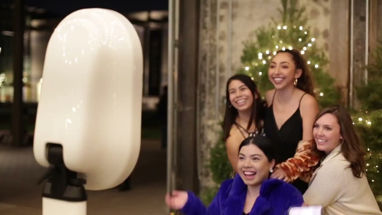 Guests laughing and posing in front of a winter-themed photo booth at a corporate holiday party in Metro Detroit, with twinkling lights and festive props.