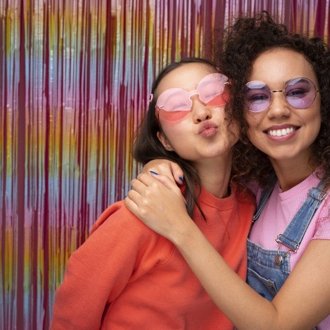 Guests laughing and posing in front of a glam photo booth with instant printouts at an outdoor birthday party.